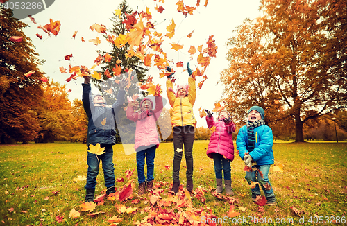 Image of happy children playing with autumn leaves in park