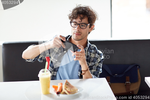 Image of man with smartphone photographing food at cafe