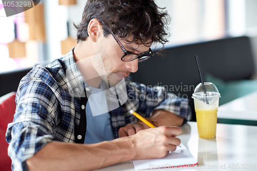 Image of man with notebook and juice writing at cafe