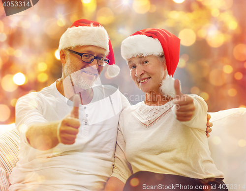 Image of senior couple in santa hats showing thumbs up