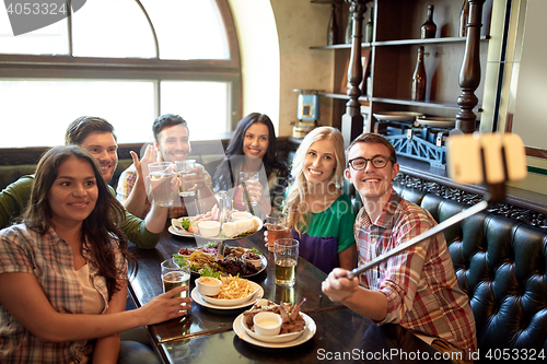 Image of happy friends with selfie stick at bar or pub