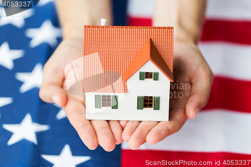 Image of close up of hands holding house over american flag