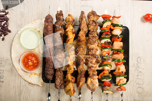 Image of set shashlik. kebab skewer, black rectangular plate. sauce and onions