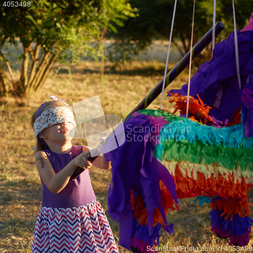 Image of Young girl at an outdoor party hitting a pinata