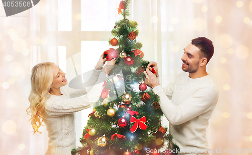 Image of happy couple decorating christmas tree at home