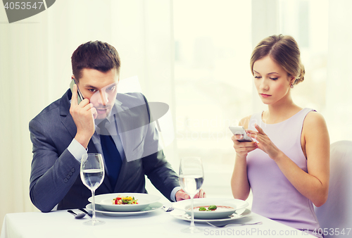Image of busy couple with smartphones at restaurant