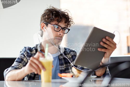 Image of man with tablet pc and earphones sitting at cafe