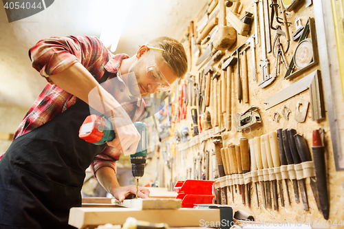 Image of carpenter with drill drilling plank at workshop