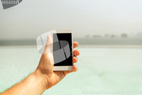 Image of close up of male hand holding smartphone on beach