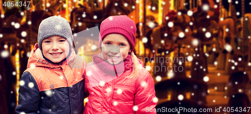Image of little girl hugging boy over snow and carousel