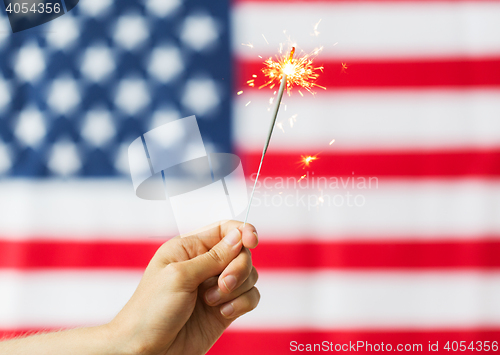 Image of close up of hand with sparkler over american flag