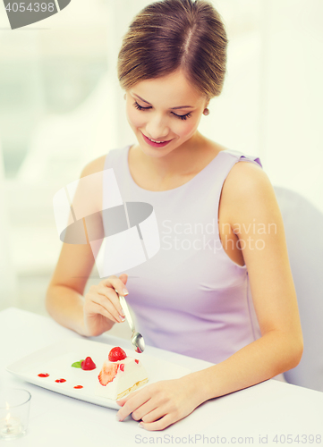 Image of smiling young woman eating dessert at restaurant