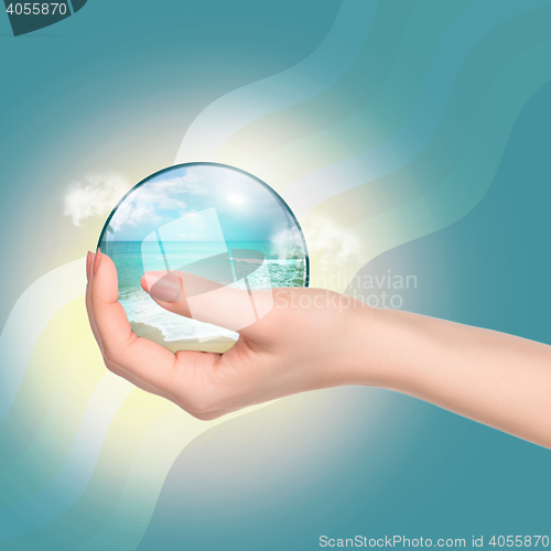 Image of Hand holding crystal ball with beach and sea