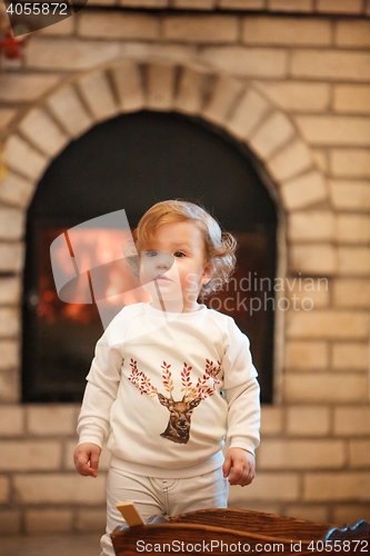 Image of The little girl standing at home against fireplace