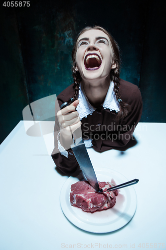 Image of Bloody Halloween theme: crazy girl with a knife, fork and meat