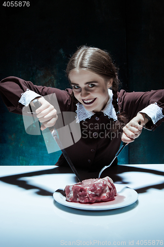 Image of Bloody Halloween theme: crazy girl with a knife, fork and meat