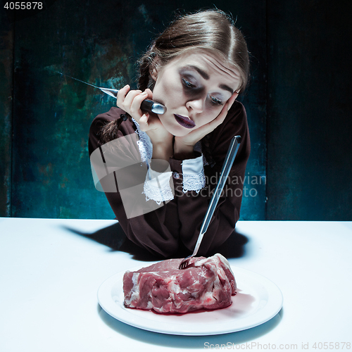 Image of Bloody Halloween theme: crazy girl with a knife, fork and meat