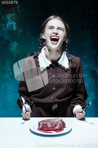 Image of Bloody Halloween theme: crazy girl with a knife, fork and meat