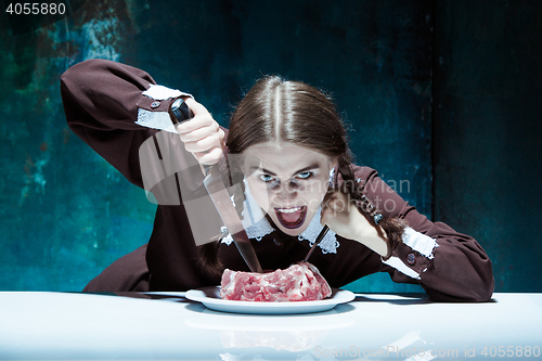 Image of Bloody Halloween theme: crazy girl with a knife, fork and meat