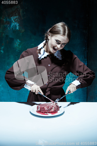 Image of Bloody Halloween theme: crazy girl with a knife, fork and meat