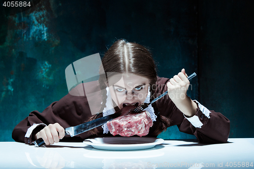 Image of Bloody Halloween theme: crazy girl with a knife, fork and meat