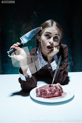 Image of Bloody Halloween theme: crazy girl with a knife, fork and meat