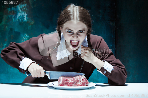 Image of Bloody Halloween theme: crazy girl with a knife, fork and meat