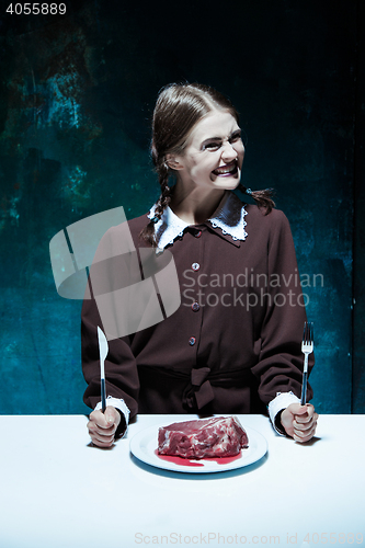 Image of Bloody Halloween theme: crazy girl with a knife, fork and meat