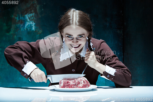 Image of Bloody Halloween theme: crazy girl with a knife, fork and meat