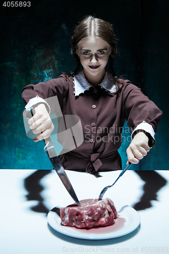 Image of Bloody Halloween theme: crazy girl with a knife, fork and meat