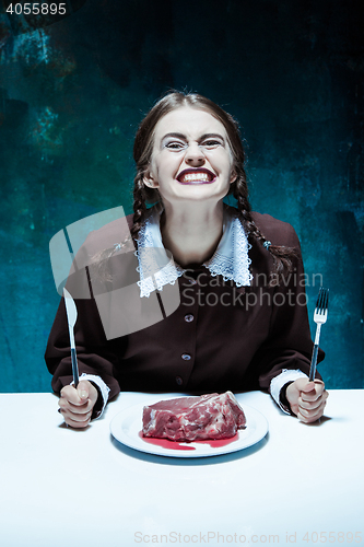 Image of Bloody Halloween theme: crazy girl with a knife, fork and meat