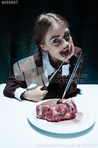 Image of Bloody Halloween theme: crazy girl with a knife, fork and meat