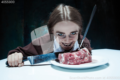 Image of Bloody Halloween theme: crazy girl with a knife, fork and meat