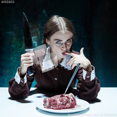Image of Bloody Halloween theme: crazy girl with a knife, fork and meat