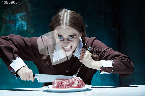 Image of Bloody Halloween theme: crazy girl with a knife, fork and meat