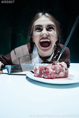 Image of Bloody Halloween theme: crazy girl with a knife, fork and meat