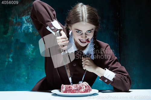 Image of Bloody Halloween theme: crazy girl with a knife, fork and meat