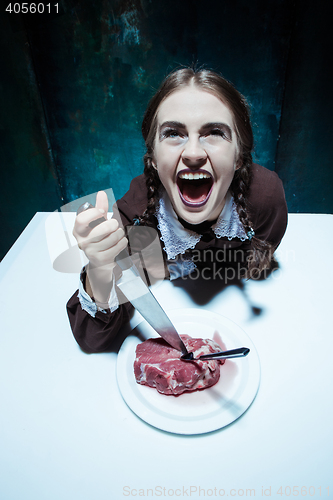 Image of Bloody Halloween theme: crazy girl with a knife, fork and meat