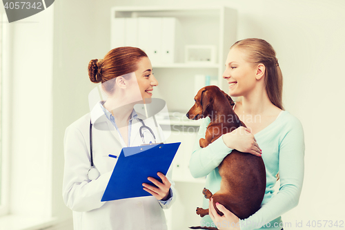 Image of happy woman with dog and doctor at vet clinic