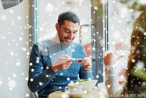 Image of happy couple picturing food by smartphone at cafe