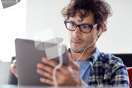 Image of man with tablet pc and earphones sitting at cafe