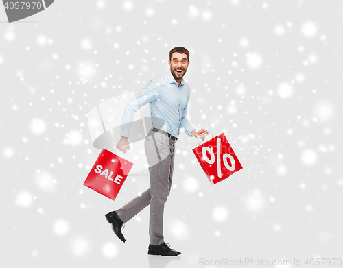 Image of smiling man with red shopping bags over snow