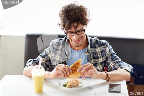 Image of happy man eating sandwich at cafe for lunch