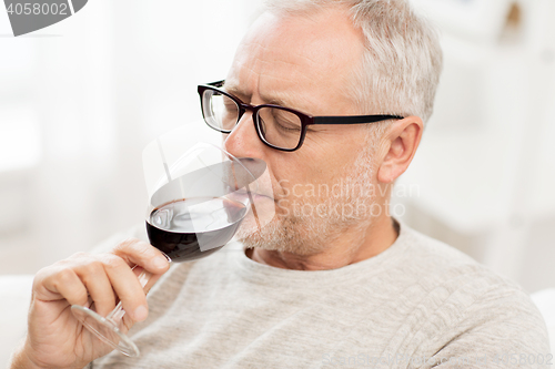 Image of senior man drinking red wine from glass at home