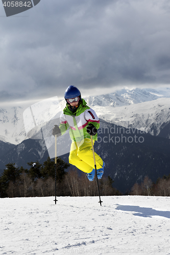 Image of Young skier jump with ski poles in sun winter mountains and clou
