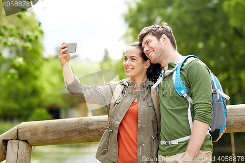 Image of couple with backpacks taking selfie by smartphone