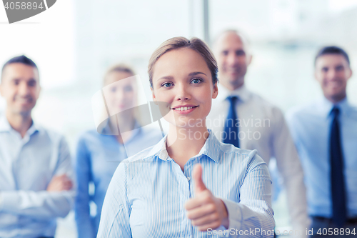 Image of smiling businesswoman showing thumbs up in office