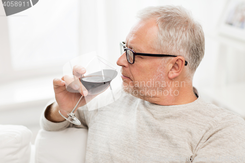 Image of senior man drinking red wine from glass at home