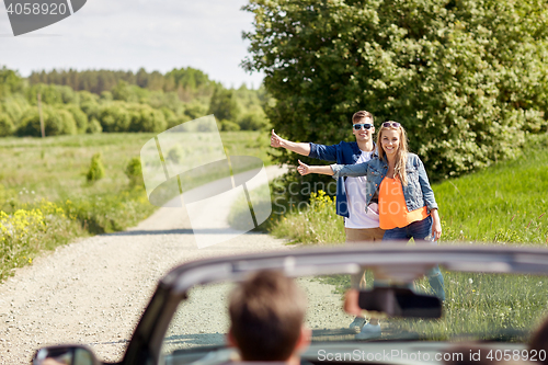 Image of couple hitchhiking and stopping car on countryside