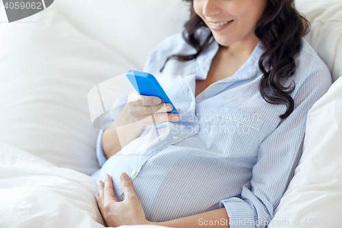 Image of close up of pregnant woman with smartphone in bed
